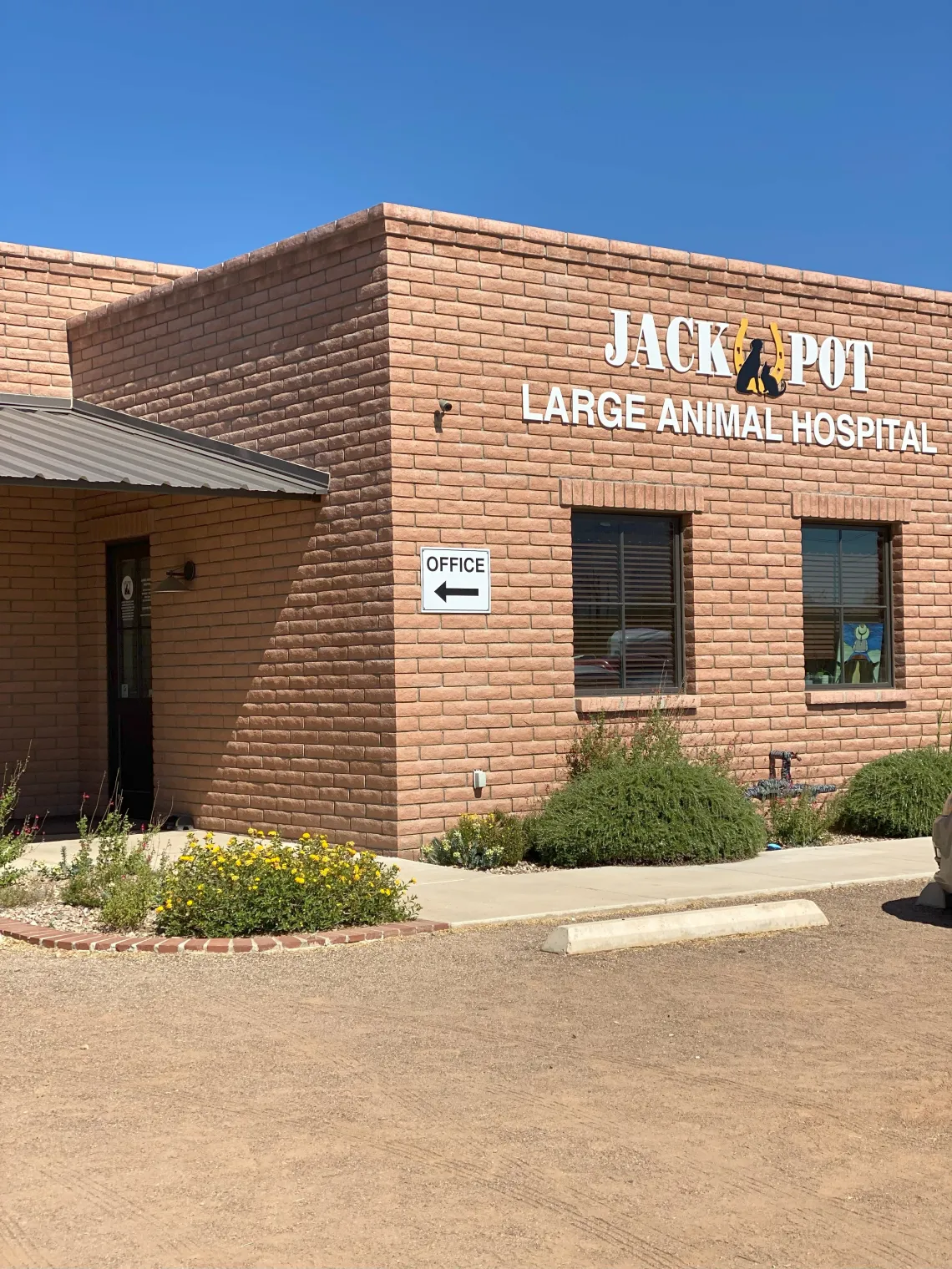 The exterior of Jackpot Veterinary Center: a brick building with flowers in front and signs reading "Jackpot Large Animal Hospital."