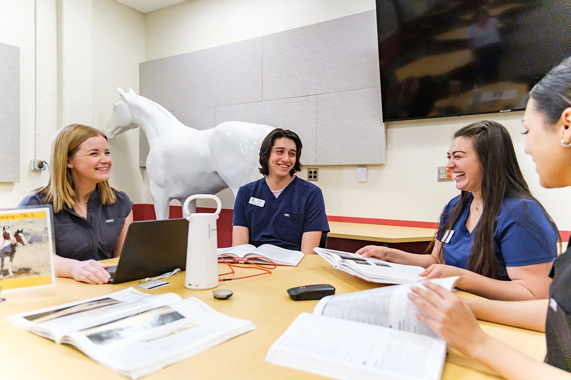 Students sitting around a table smiling and laughing. 